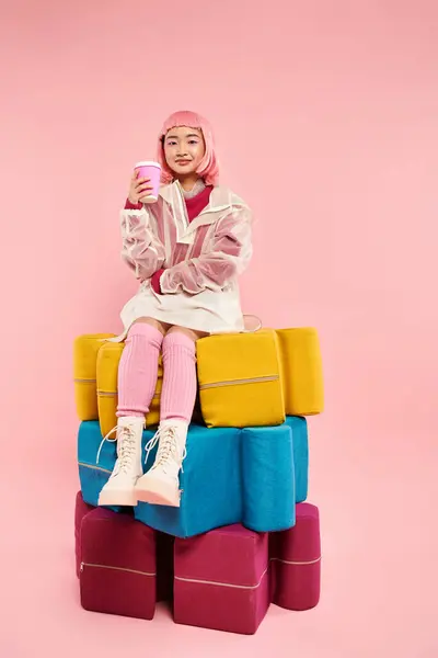 Pretty young woman with pink hair sitting on larges puzzles with cup of coffee on vibrant background — Stock Photo