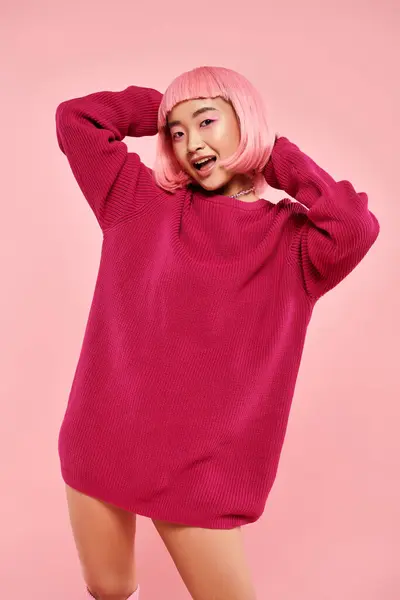 Lindo asiático joven mujer con rosa pelo y maquillaje en Grande suéter contra vibrante fondo - foto de stock