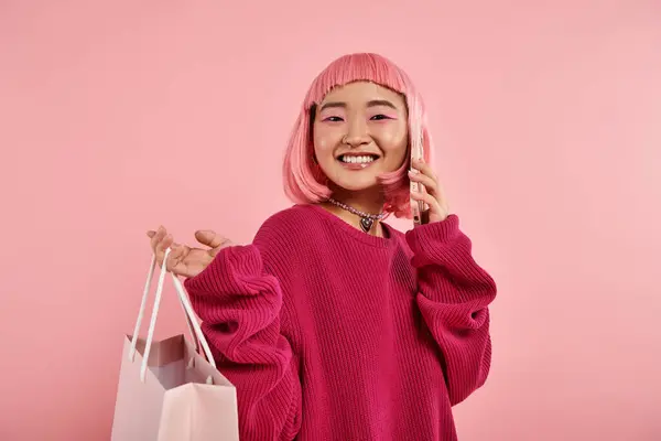 Smiling young woman calling of smartphone and holding packet over shoulder on pink background — Stock Photo