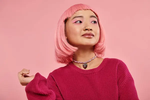 Encantadora mujer joven asiática con collar de perlas y pelo rosa mirando a un lado sobre fondo vibrante - foto de stock