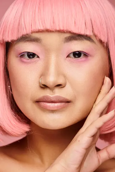 Vicino di bella asiatico donna in suo 20s con naso piercing toccare a faccia su vibrante sfondo — Foto stock
