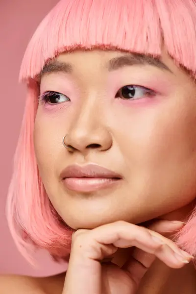 Primer plano de seductora chica asiática con el pelo rosa de apoyo a la barbilla con la mano y mirando a un lado - foto de stock