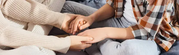 Une mère et sa fille assises sur un canapé confortable, se tenant la main et profitant de moments de qualité ensemble à la maison. — Photo de stock