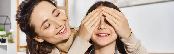 A woman, embracing her child, covers her eyes with her hands in a moment of playful intimacy and connection at home. — Stock Photo