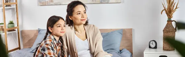 Una mujer sentada cerca de una joven en una cama acogedora, compartiendo momentos sentidos juntos en casa. - foto de stock