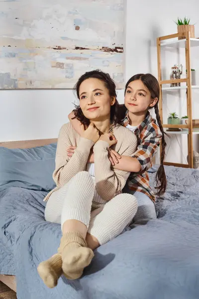 Una madre e una figlia sedute insieme su un letto, che condividono un momento speciale e amorevole a casa. — Foto stock