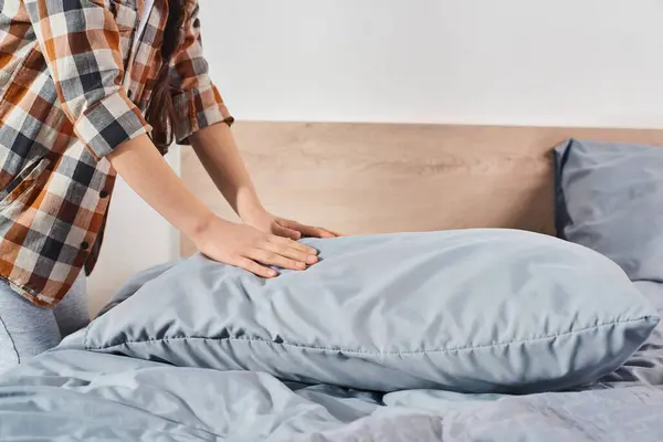 Человек, вероятно, девушка, мягко кладет подушку на аккуратно заправленную кровать в теплую, уютную спальню. — стоковое фото