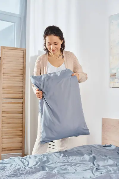 Una mujer arregla amorosamente una manta azul sobre una cama acogedora, creando un ambiente tranquilo y cálido para su hija. - foto de stock