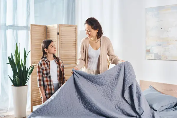 Жінка і дівчина, що стоїть мирно перед ліжком, вкритим синьою ковдрою, насолоджуються якісним часом разом вдома. — стокове фото