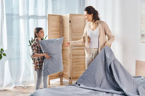 Жінка стоїть поруч з маленькою дівчинкою, що тримає подушку, розділяючи тихий і спокійний момент вдома. — стокове фото