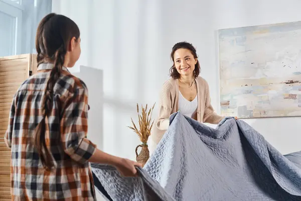 A woman stands next to a young girl holding a cozy blanket, sharing a moment of love and comfort at home. — Stock Photo