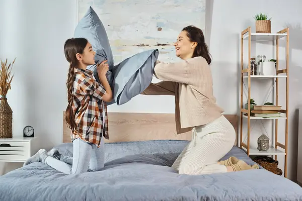 Una mujer y una niña están jugando felices juntas en una cama en casa, uniéndose y creando recuerdos preciados.. - foto de stock