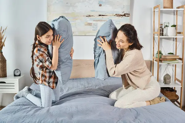 Una madre sentada en una cama junto a su pequeña hija, compartiendo un divertido momento juntos en casa. - foto de stock