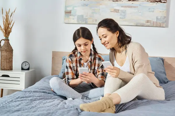 Mother and daughter, sit on a bed, engrossed in a cell phone, sharing a moment of connection. — Stock Photo