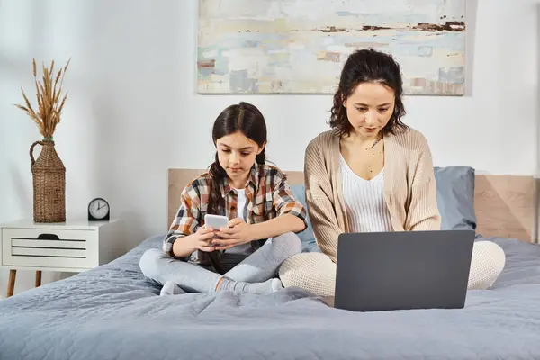 Mother and daughter, sitting on a bed, focused on a laptop screen, sharing a special moment together at home. — Stock Photo