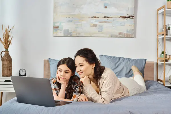 Une mère et sa fille partagent un moment de qualité ensemble, allongées sur un lit et regardant un écran d'ordinateur portable. — Photo de stock