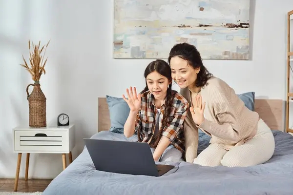 Madre e hija, compartiendo una computadora portátil mientras están sentadas en una cama acogedora en un entorno hogareño. - foto de stock