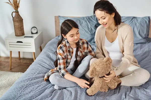 A mother and daughter sit together on a bed, deep in conversation while holding a teddy bear. — Stock Photo
