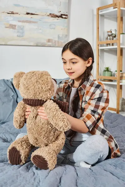 Ein Mädchen sitzt auf ihrem Bett, hält zärtlich einen Teddybär in der Hand und verbringt Zeit miteinander zu Hause. — Stockfoto