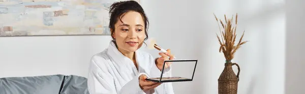 A brunette woman in a white robe holding eye shadows palette in a cozy setting. — Stock Photo