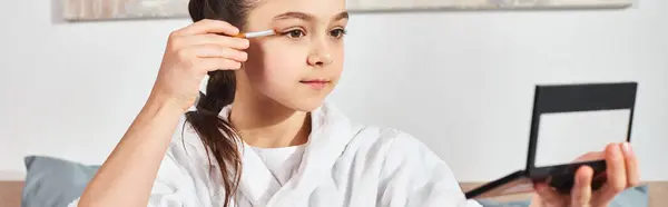 Una ragazza bruna in accappatoio bianco si siede su un letto, applicando il trucco al suo viso. — Foto stock