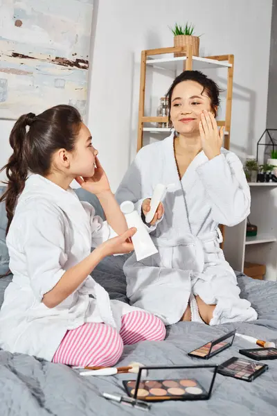 Eine brünette Mutter und ihre Tochter in weißen Bademänteln sitzen zusammen auf einem Bett und teilen sich eine besondere Bindung und Zeit der Qualität. — Stockfoto