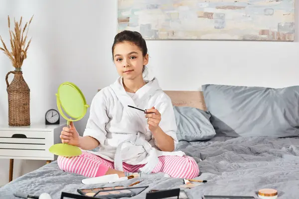 Une fille en peignoir blanc s'assoit sur un lit, tenant un miroir, exprimant curiosité et innocence. — Photo de stock