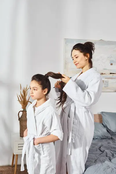 A brunette mother and her little daughter, both in white bath robes, standing together in a heartwarming moment. — Stock Photo