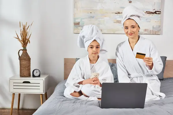 Mother and daughter in white bath robes, sitting on a bed, sharing a special moment together. — Stock Photo