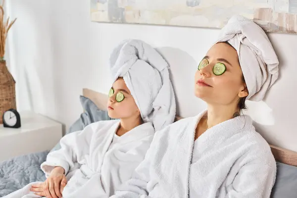 Due donne brune in accappatoi bianchi che godono di un trattamento spa con toppe di cetriolo sugli occhi. — Foto stock