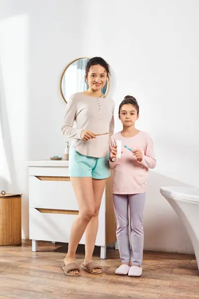 Брюнетка стоїть зі своєю дев'ятнадцятьма донькою у сучасній ванній кімнаті, беручи участь у процедурах краси та гігієни разом. — стокове фото