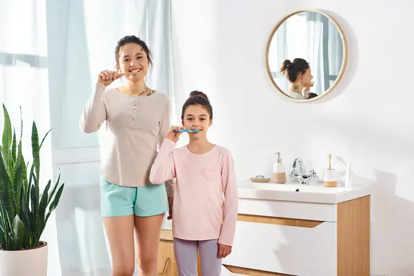 A brunette woman and her preteen daughter brush their teeth in a modern bathroom as part of their beauty and hygiene routine. — Stock Photo