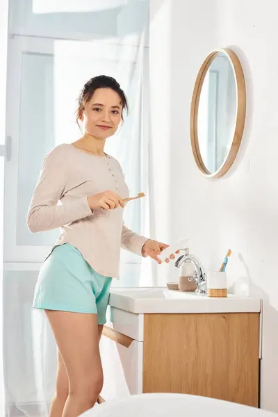 Eine brünette Frau steht vor einem modernen Waschbecken im Badezimmer und übt sich in Schönheit und Hygiene. — Stockfoto