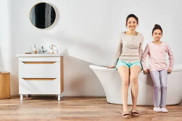 Une femme brune et sa fille préadolescente se détendre et discuter tout en étant assis sur une baignoire dans une salle de bain moderne. — Photo de stock