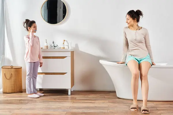 Una donna bruna si trova accanto alla sua figlia preadolescente in un bagno moderno, impegnandosi in routine di bellezza e igiene. — Foto stock