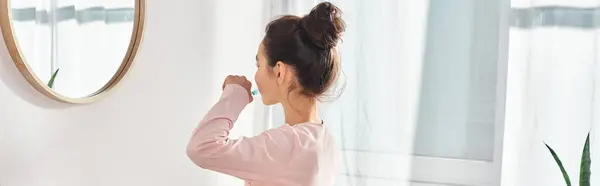 Ein brünettes Mädchen steht in einem modernen Badezimmer und putzt sich die Zähne vor einem Spiegel. — Stockfoto