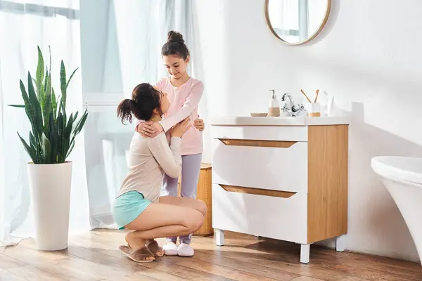 Uma mulher morena e sua filha pré-adolescente abraçando em um banheiro moderno durante sua rotina de beleza e higiene. — Fotografia de Stock