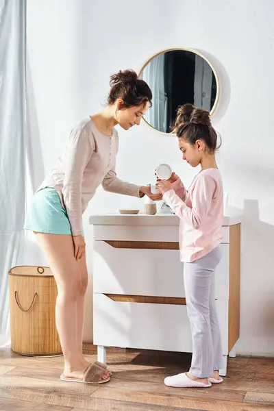 A brunette woman and her preteen daughter are standing in front of a mirror in a modern bathroom, engaging in their beauty routine. — Stock Photo