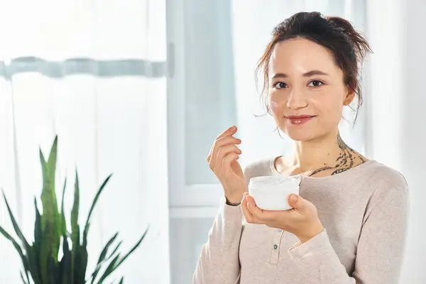 Uma mulher morena elegante segurando um pote de creme na mão, desfrutando de um momento de relaxamento e indulgência. — Fotografia de Stock