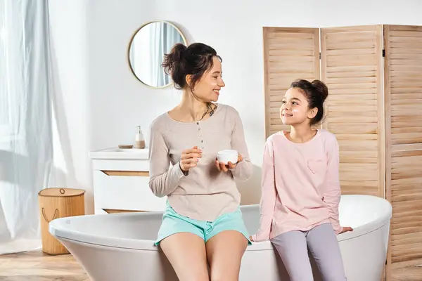 Una donna bruna e sua figlia preadolescente si rilassano in una vasca da bagno in un bagno moderno, godendo di una routine di bellezza e igiene. — Foto stock