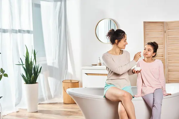 A brunette woman lovingly apply cream on her preteen daughters face in a modern bathroom during their beauty and hygiene routine. — Stock Photo