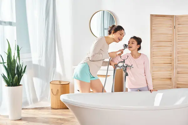 Una donna bruna e sua figlia preadolescente si trovano l'una accanto all'altra in un bagno moderno durante la loro routine di bellezza e igiene.. — Foto stock