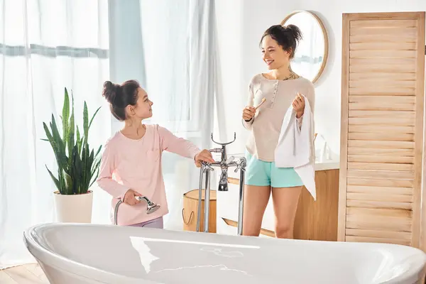 Una donna e una bambina stanno accanto a una vasca da bagno in un bagno moderno, impegnati in una routine di bellezza e igiene.. — Foto stock