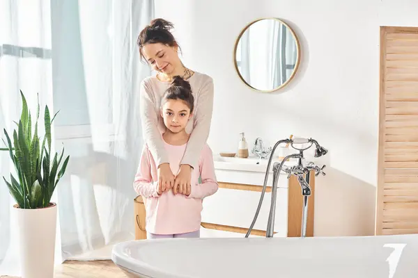 Una mujer con el pelo morena y su hija preadolescente de pie en un baño moderno, comprometida con su rutina de belleza e higiene. - foto de stock
