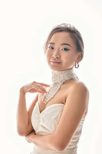 Attractive asian young woman with elegant hairstyle posing to camera and touching to necklace — Stock Photo