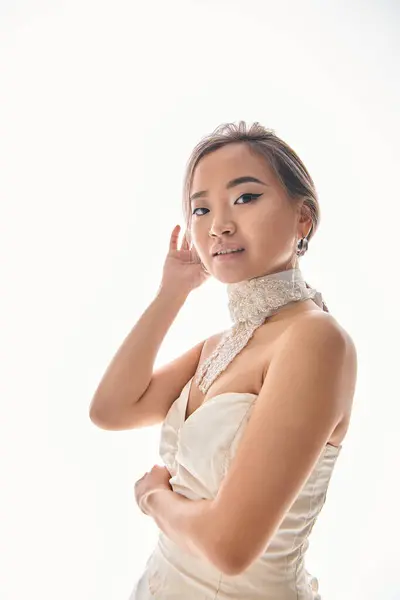 Verführerische asiatische Braut Befestigung Frisur und Blick auf die Kamera vor weißem Hintergrund — Stockfoto