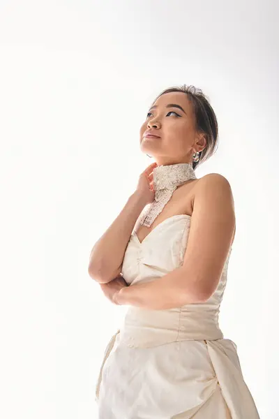 Elegante mujer asiática en 20s con collar de lujo mirando hacia arriba y tocando en el cuello - foto de stock