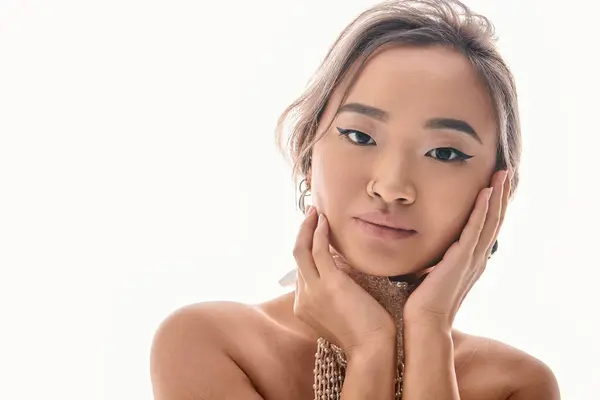 Retrato de encantadora chica asiática con collar blanco abrazo a la mejilla con las manos sobre fondo claro - foto de stock