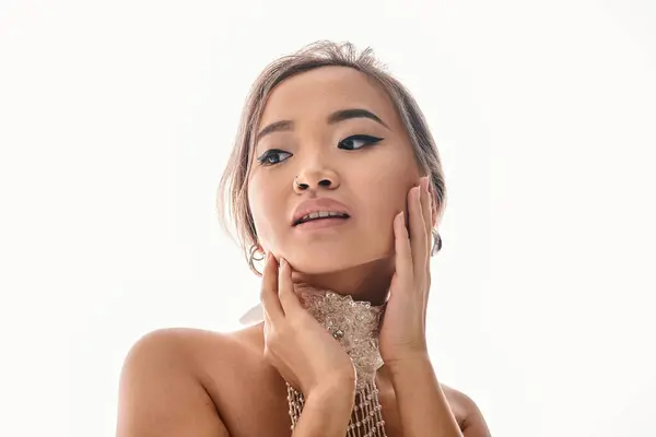 Verführerische asiatische junge Frau mit weißer Halskette Umarmung bis zur Wange mit Händen und Blick zur Seite — Stockfoto