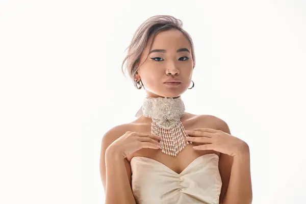 Элегантная азиатская женщина с белым ожерельем касаясь декольте с руками на светлом фоне — стоковое фото